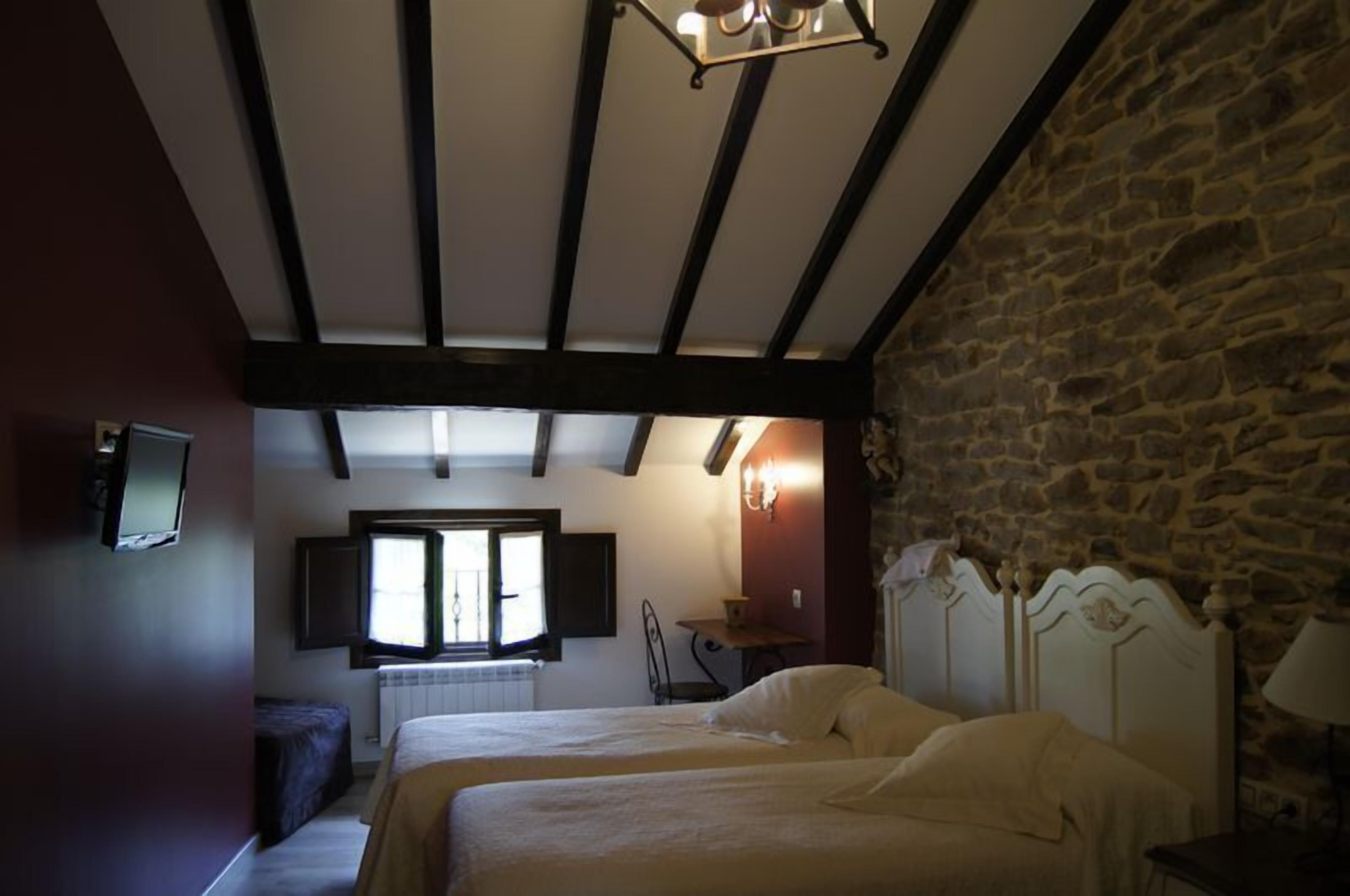 Un dormitorio con dos camas, una pared de piedra, techo de madera y una ventana con contraventanas.