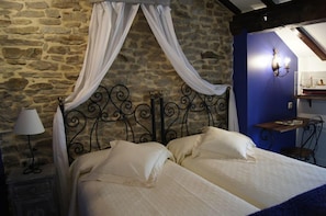 A room with a stone wall, a bed with white bedding, a nightstand with a lamp, and a blue accent wall with a wall sconce. - Hotel Rural Casa Encanto (Espinosa de los Monteros)