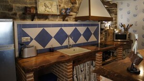 Een keuken met een stenen muur, blauw-witte tegels, een houten aanrecht, een spoelbak, een broodrooster, een magnetron en een hangende lamp.