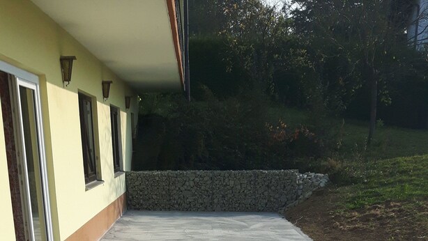 A paved patio area with a stone wall and a building with windows. - Gasthaus und Pension Stanek (Hofkirchen)