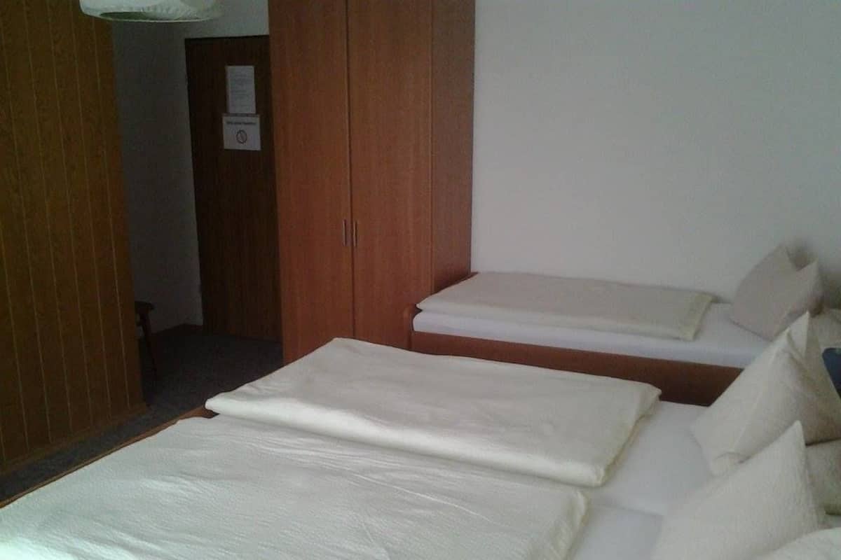 A hotel room with a bed, a wooden wardrobe, and a small table.