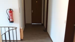 A hallway with a wooden floor, a fire extinguisher mounted on the wall, and a door at the end. - Gasthaus und Pension Stanek (Hofkirchen)