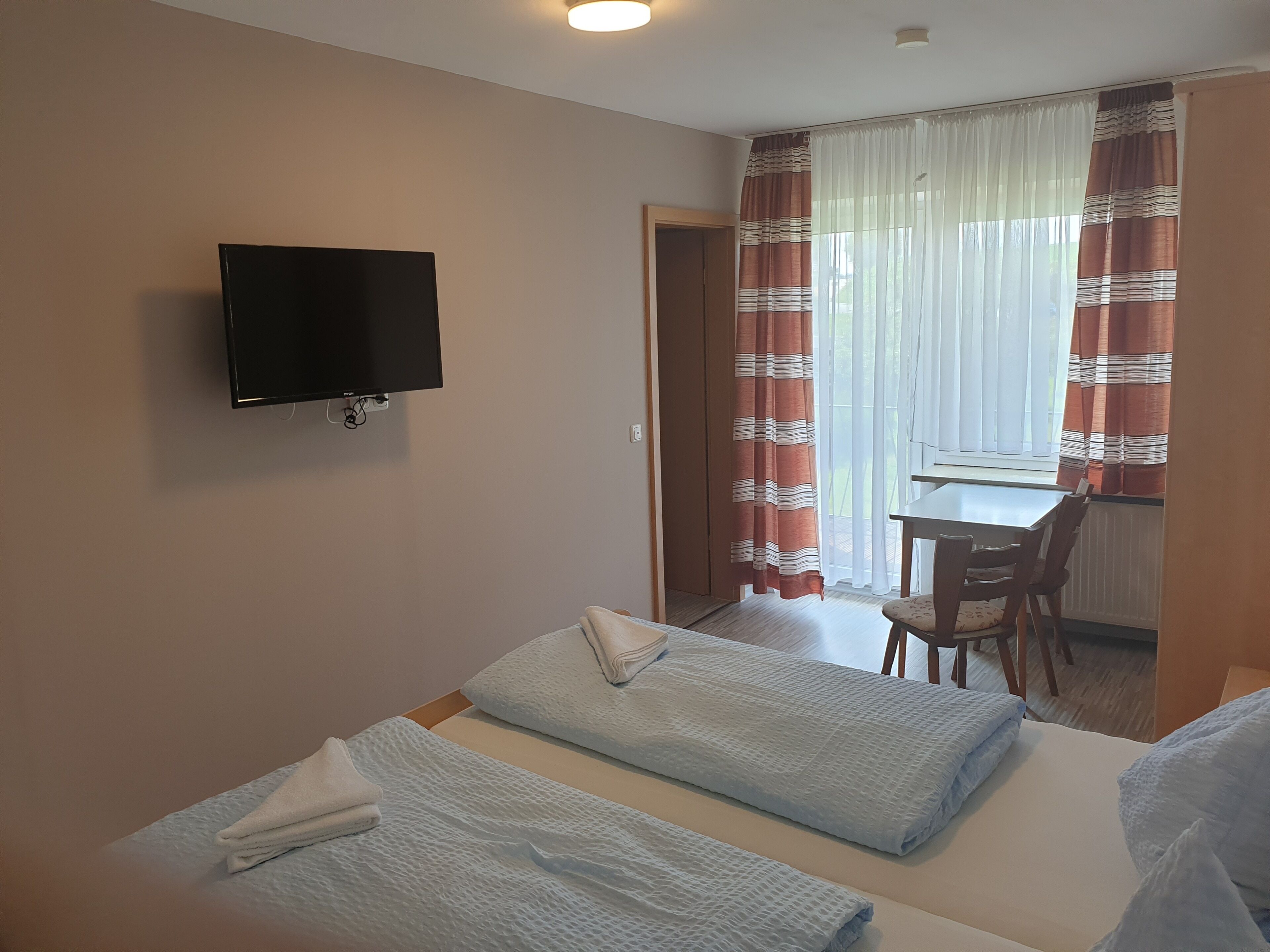 Quarto de hotel com duas camas, televisão, escrivaninha e uma cadeira.