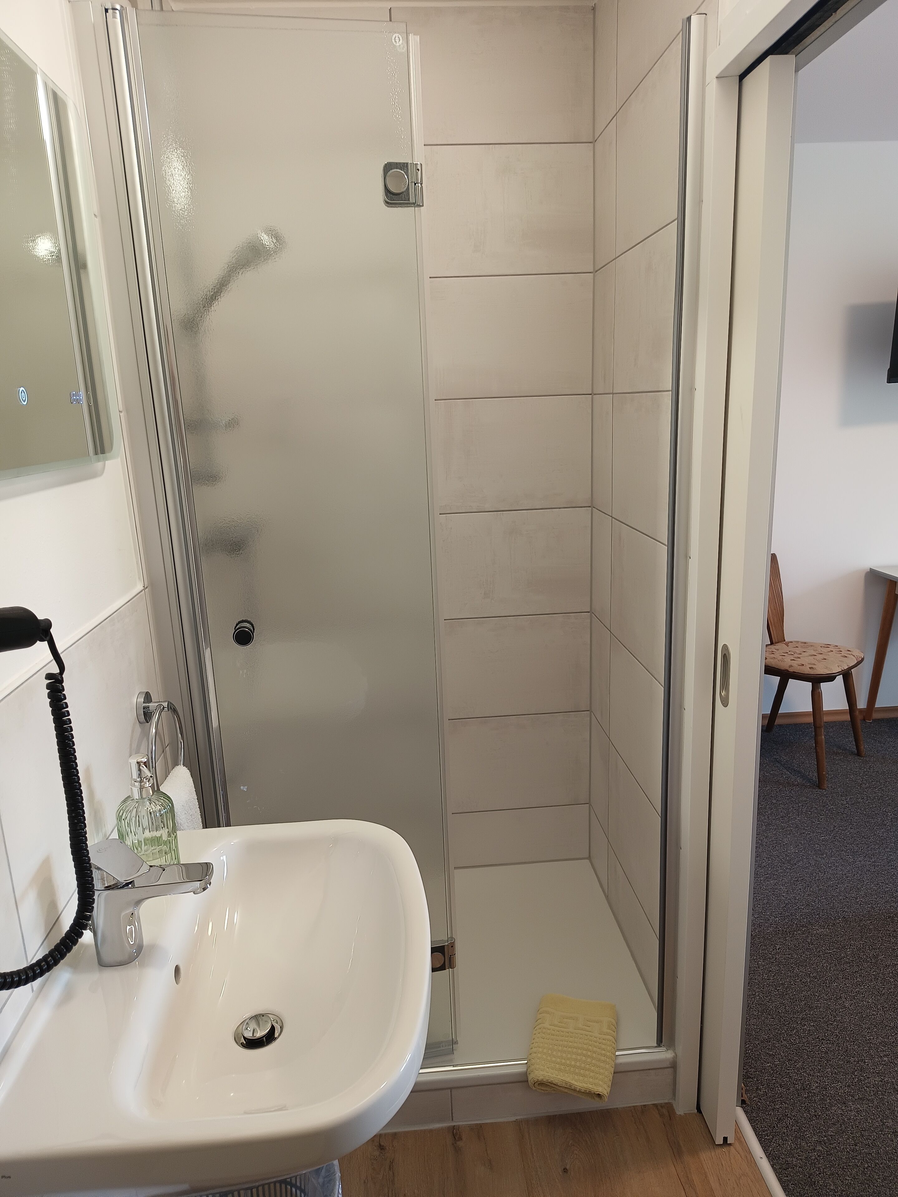 A bathroom with a white sink, a glass shower enclosure, and a wooden floor.