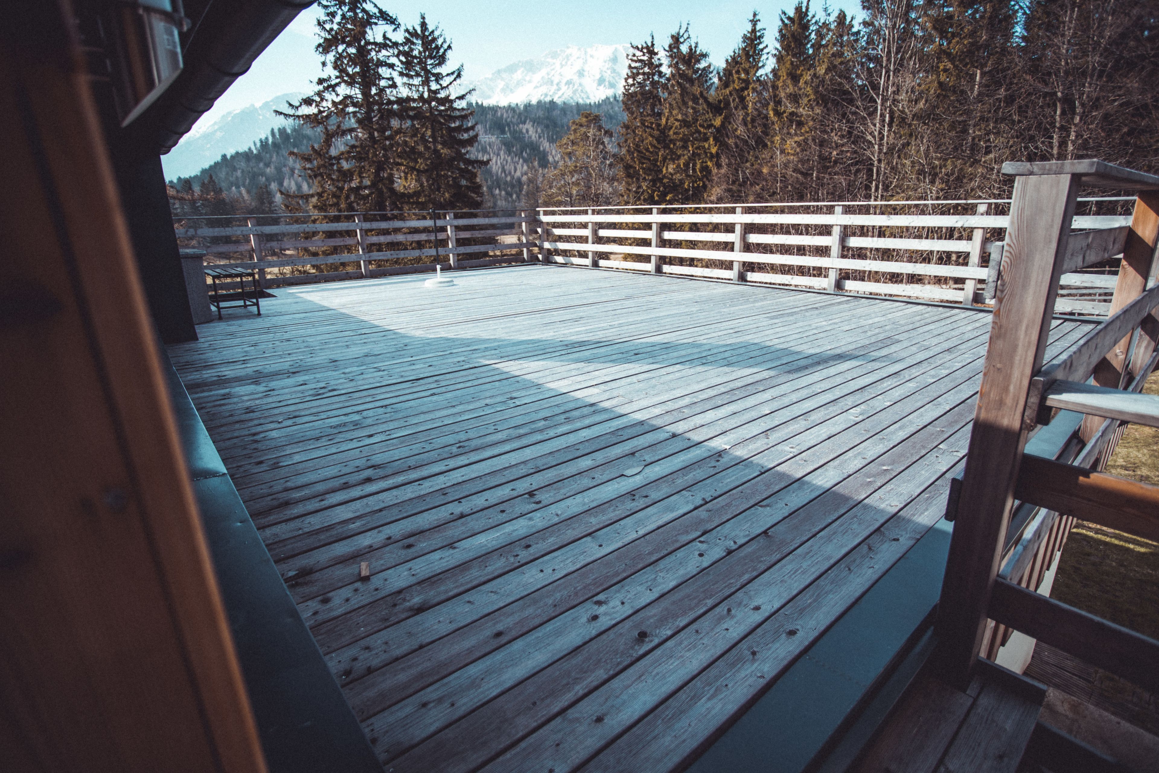 A wooden deck with a railing, benches, and a view of a forest and mountains.