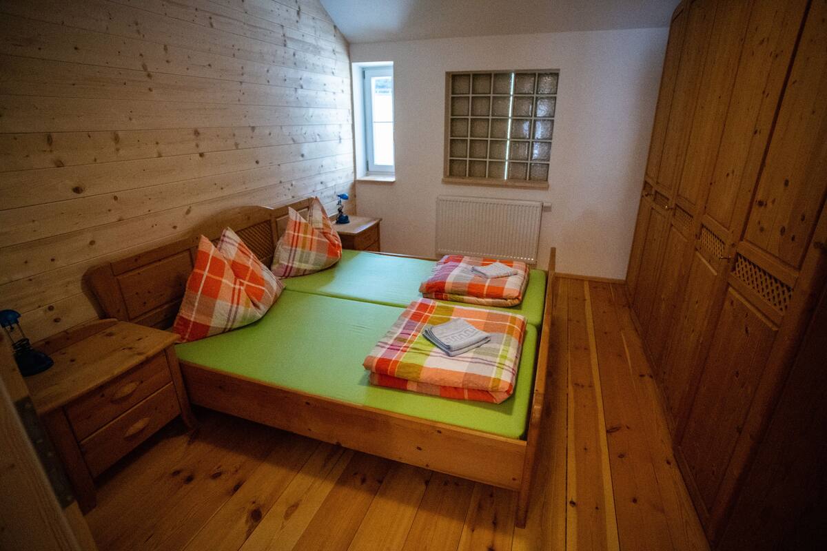 Um quarto pequeno com painéis de madeira, uma cama de solteiro, uma mesa de cabeceira, uma janela e um radiador.
