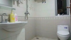 Un baño pequeño con un lavamanos blanco, dos botellas de jabón, un inodoro y un cabezal de ducha.