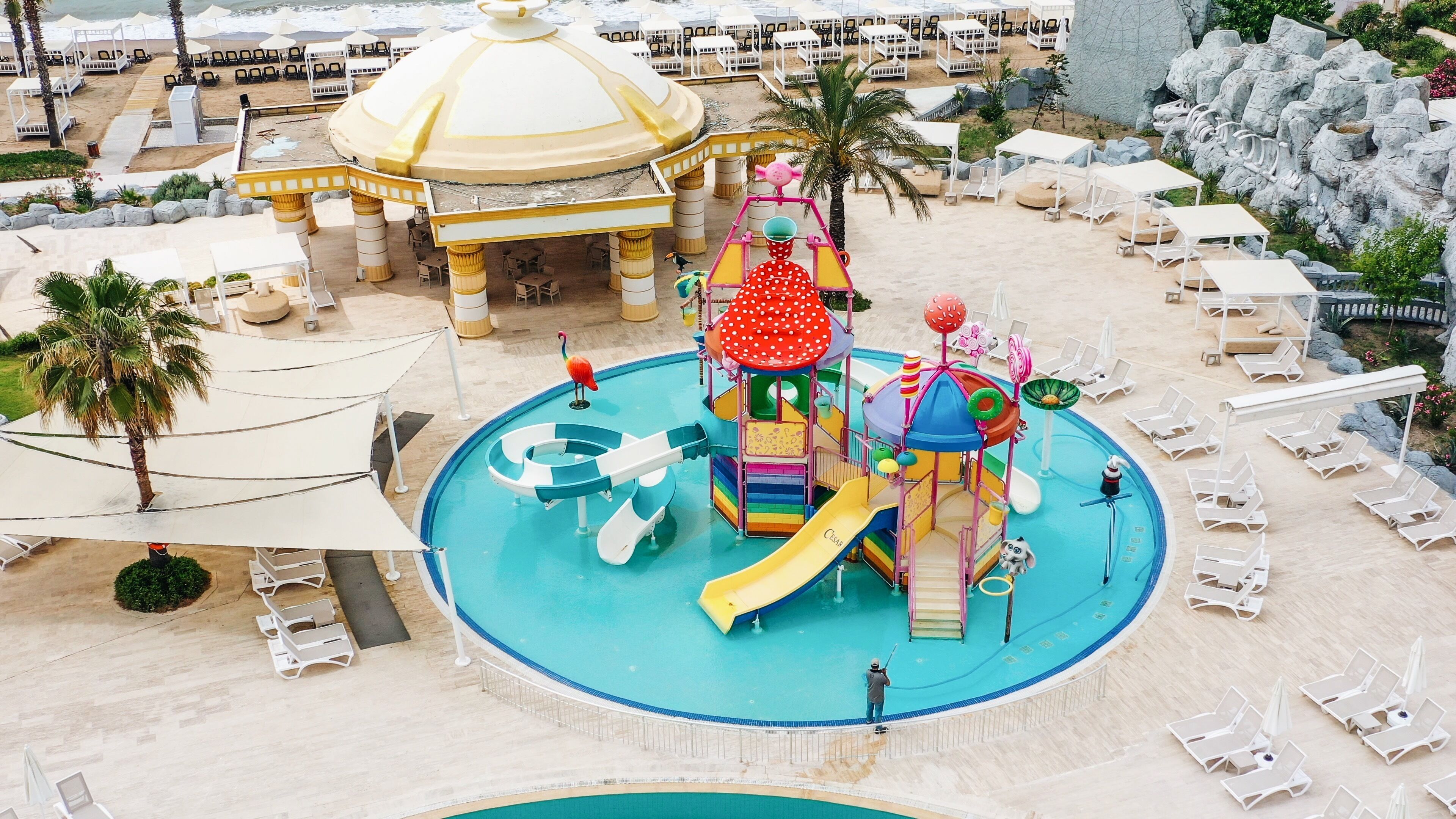 A water park with a large slide, play structures, and lounge areas with umbrellas.