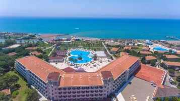 Un grande hotel con piscina centrale, numerosi balconi e vista sul mare.