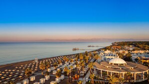 Un resort en la playa con filas de tumbonas y sombrillas, una estructura abovedada central y un muelle que se adentra en el mar.