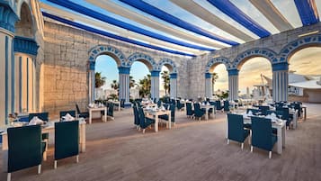 Un amplio espacio exterior para comer con arcos de piedra, toldos azul y blanco a rayas, y mesas y sillas ordenadas.