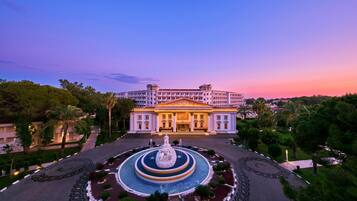 Un hotel elegante con una fuente central, rodeado de jardines cuidados y palmeras.