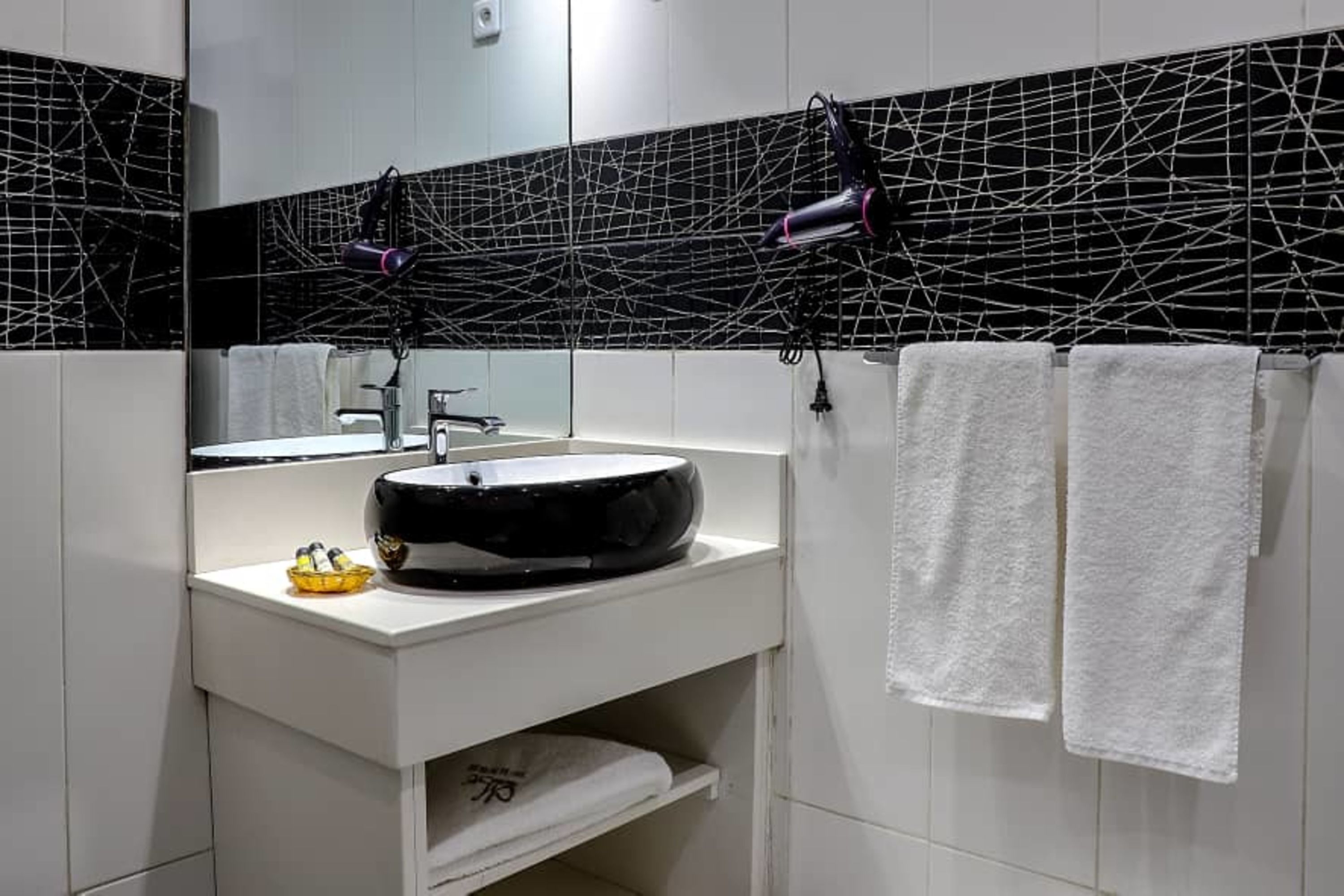 A modern bathroom with a black and white tiled backsplash, a round sink, and two white towels hanging on hooks.