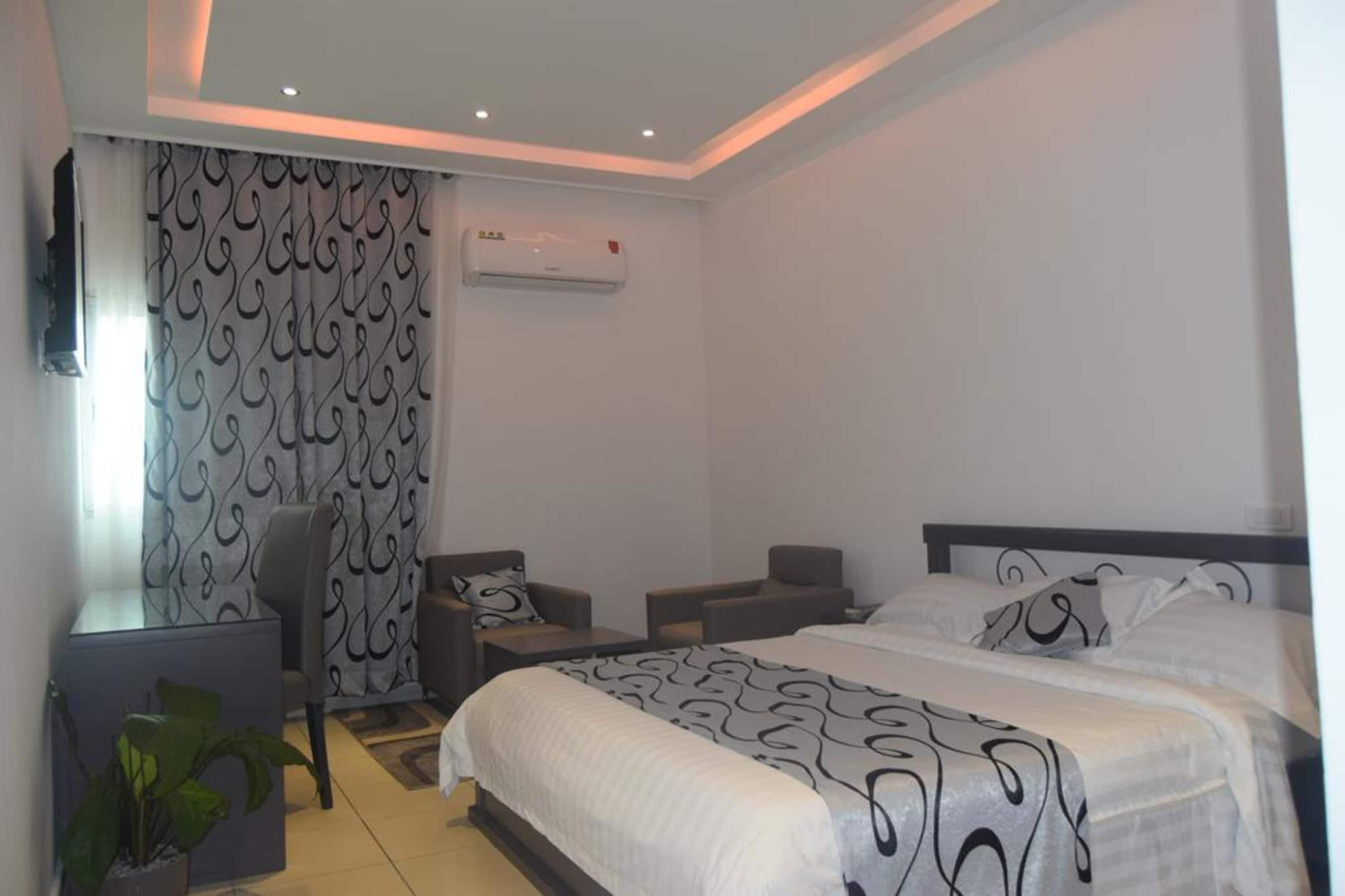 Ein modernes Hotelzimmer mit einem großen Bett, zwei Nachttischen, einem Schreibtisch, einem Stuhl und einer Zimmerpflanze.