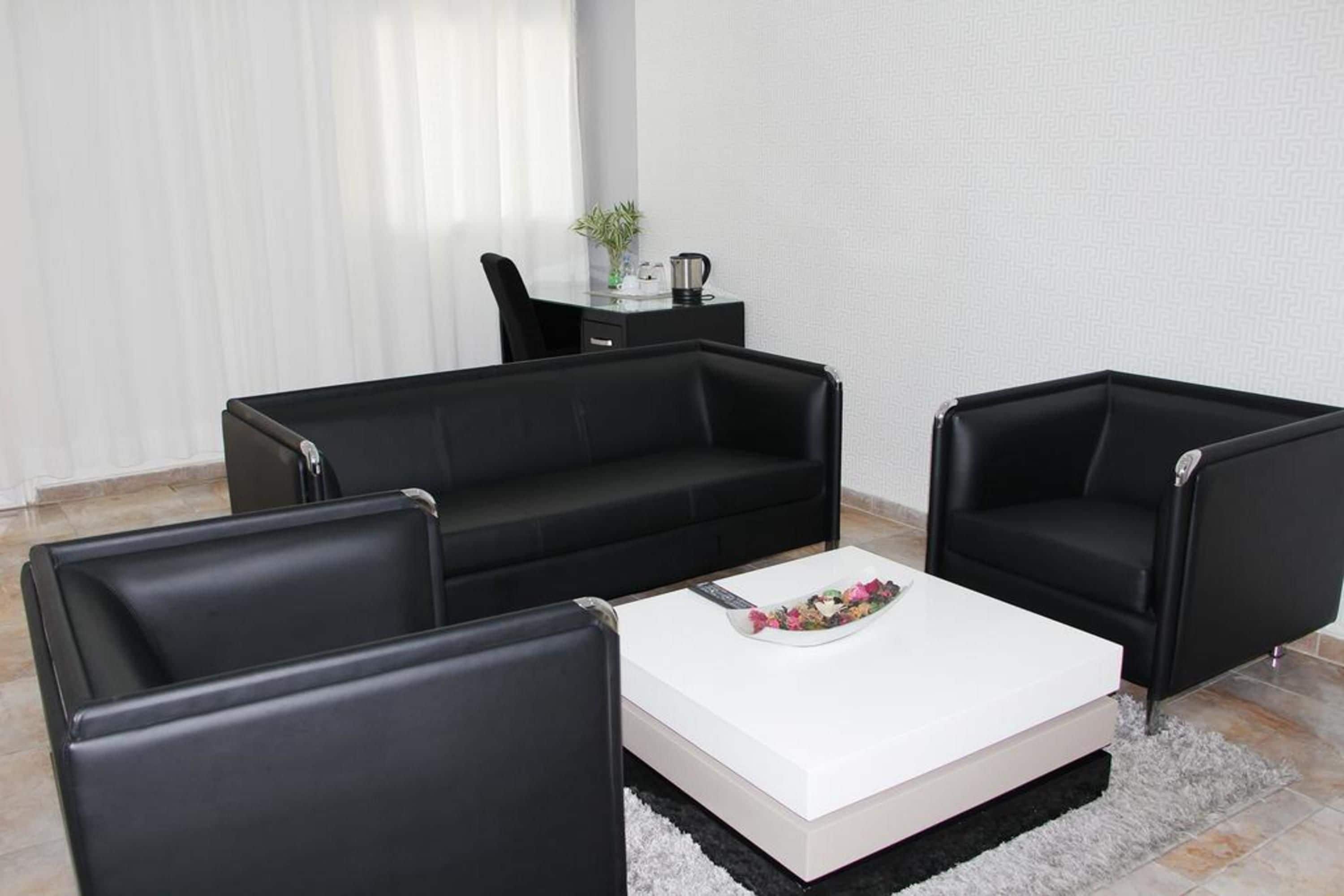 A modern living room with a black leather sofa, two black armchairs, and a white coffee table.