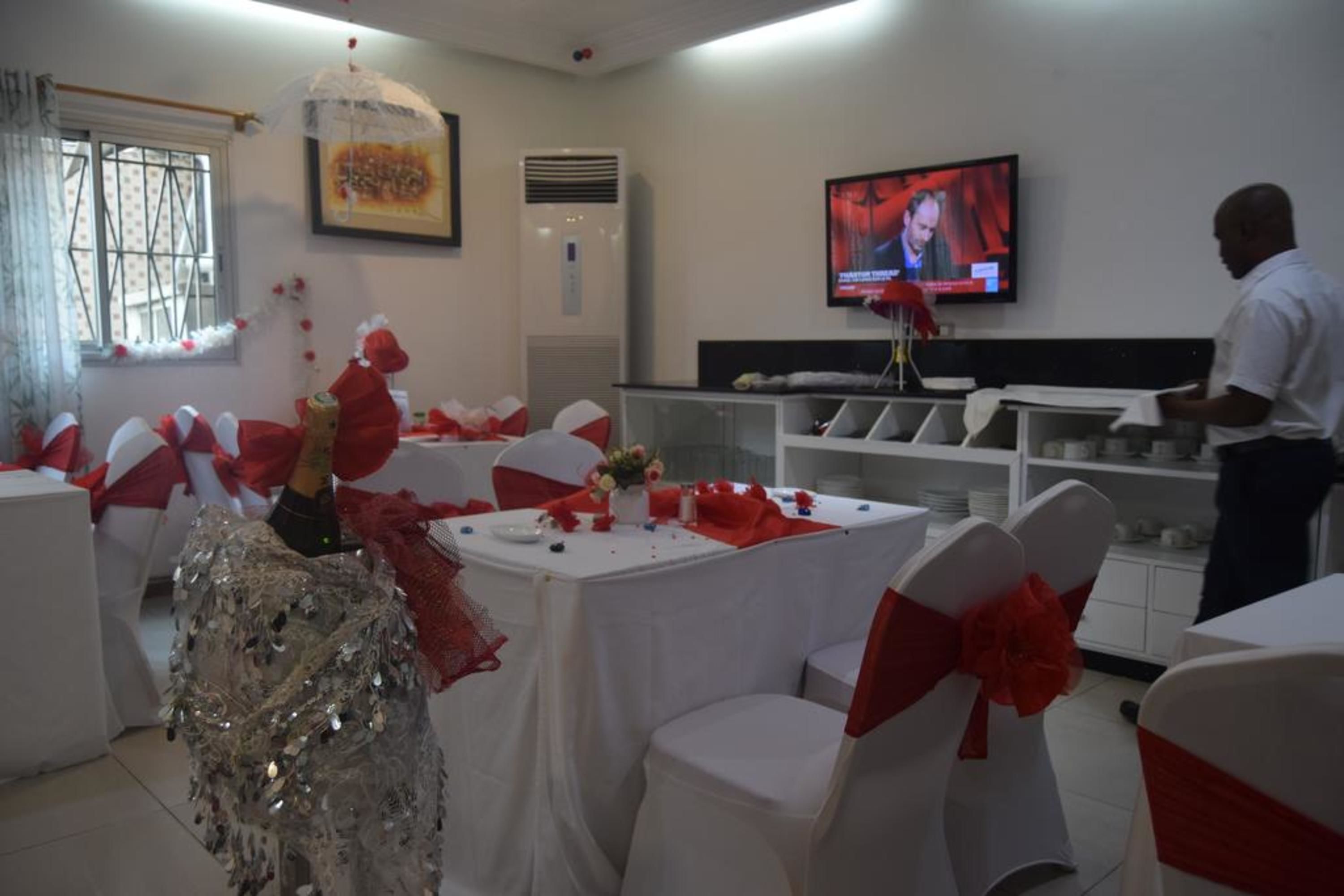A room with white tables and chairs, red sashes, and a television on the wall.