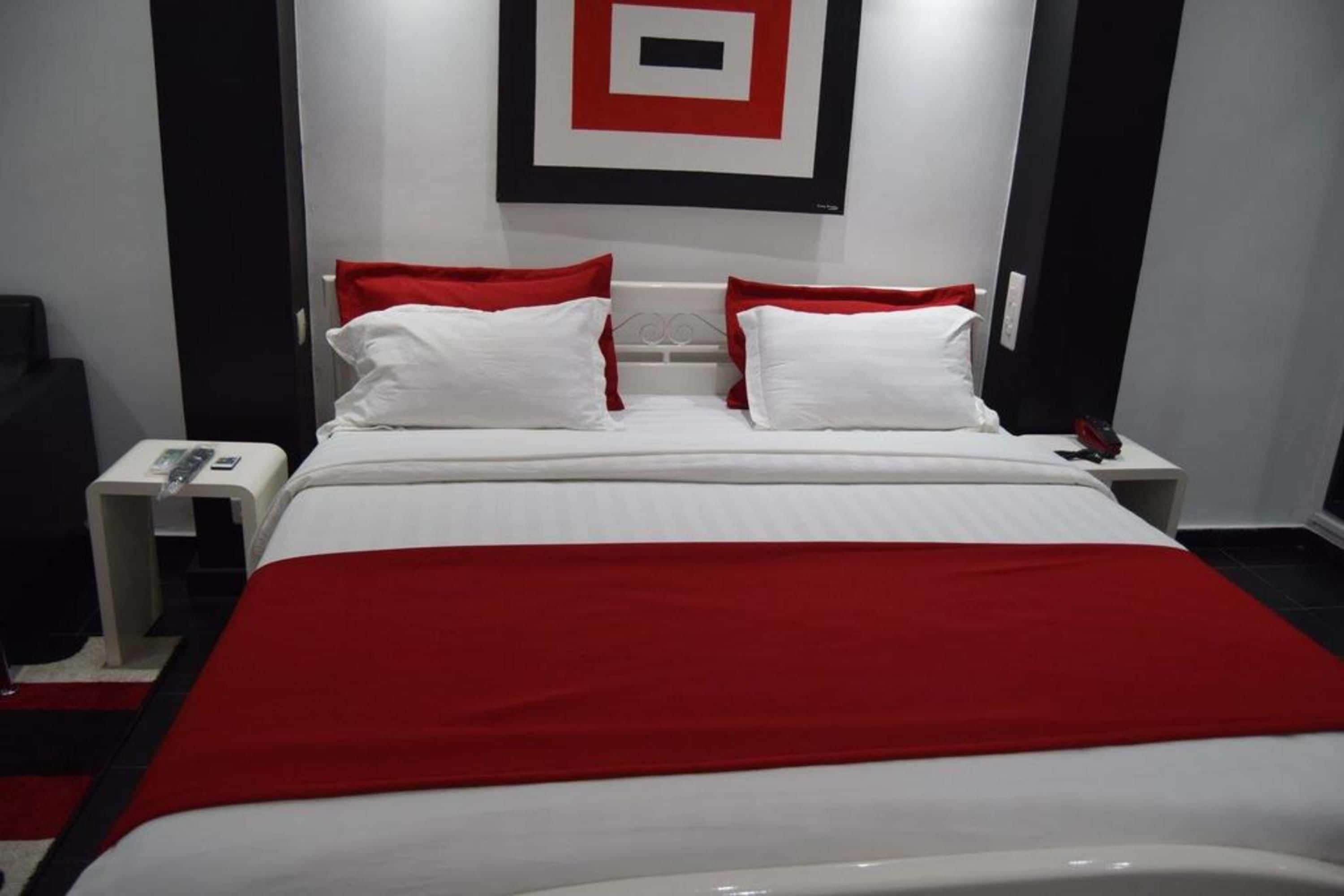 Une chambre d’hôtel comprenant un lit, deux tables de chevet, une couvre-lit rouge et blanche, et un ensemble d’oreillers rouge et blanc.