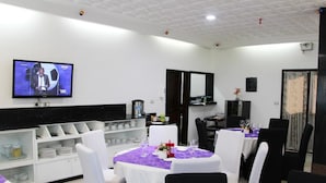 A dining area with white chairs, tables with purple tablecloths, and a television displaying a sports event. - Miliet Hotel (Abidjan)