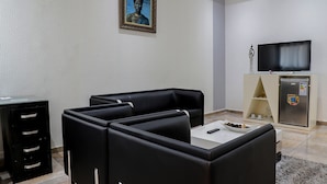 A modern living room with black leather sofas, a white coffee table, a flat-screen TV, and a refrigerator. - Miliet Hotel (Abidjan)