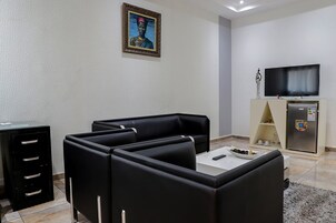 Una sala de estar moderna con sofás de cuero negro, una mesa de centro blanca, un televisor de pantalla plana y un refrigerador.