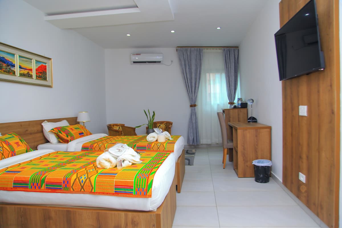 A hotel room with two beds, a desk, a TV, and a trash bin.