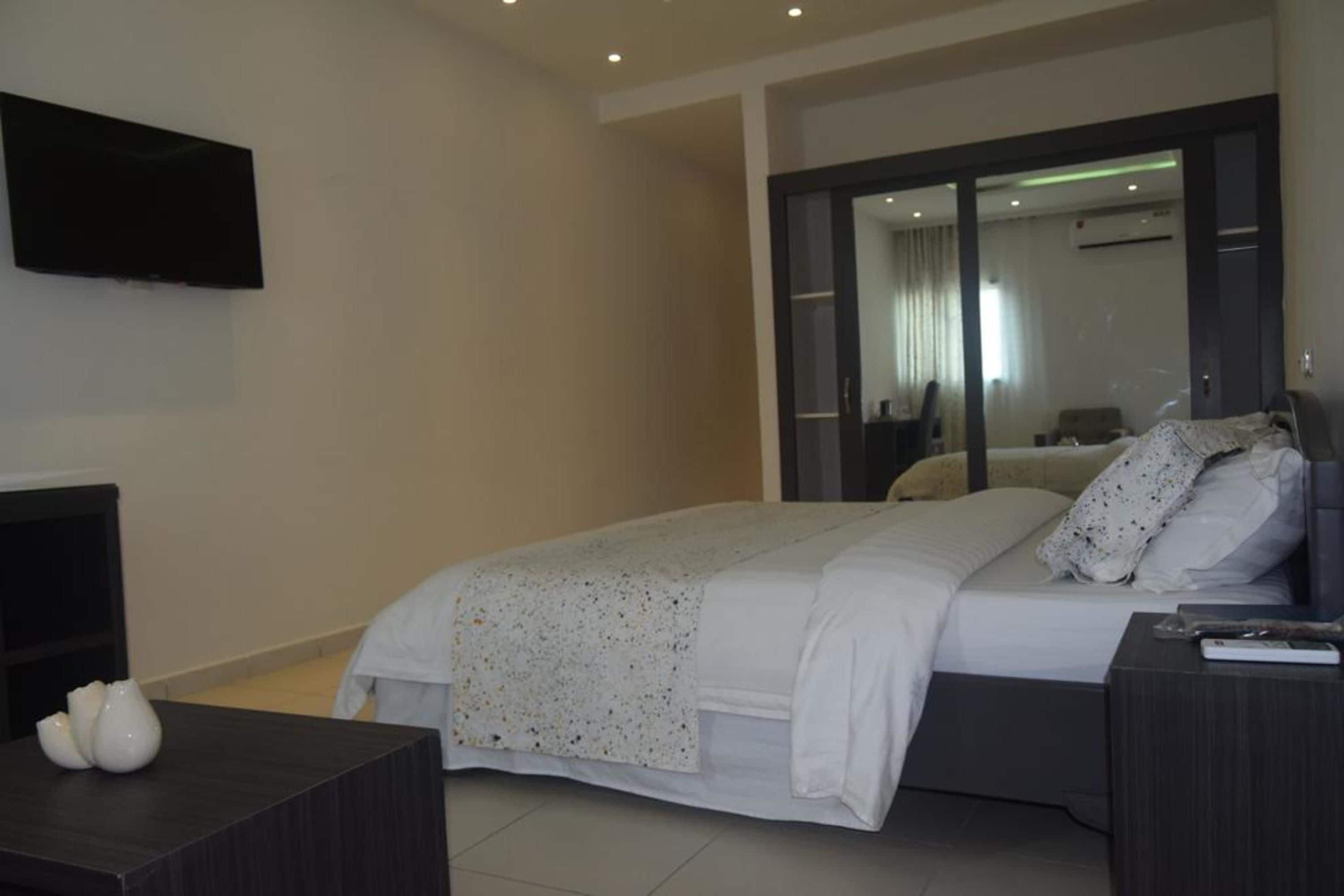 Un dormitorio moderno con cama, mesitas de noche, televisor de pantalla plana y puerta corredera de vidrio que da al baño.