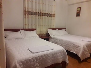 A room with two single beds, each with a wooden headboard and white bedding. There is a small table between the beds, and a painting on the wall. - Eco Hacienda Roman (Machu Picchu)