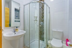 Casa de banho com chuveiro em cabine de vidro, lavatório branco e sanita.