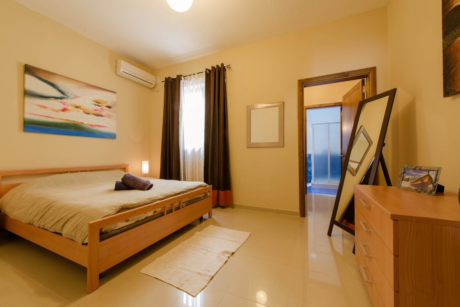 A bedroom with a wooden bed, a bedside table, a dresser, and a painting on the wall.