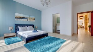 Ett sovrum med en stor säng, två sängbord, en kristallkrona och utsikt över badrummet genom en öppen dörr.