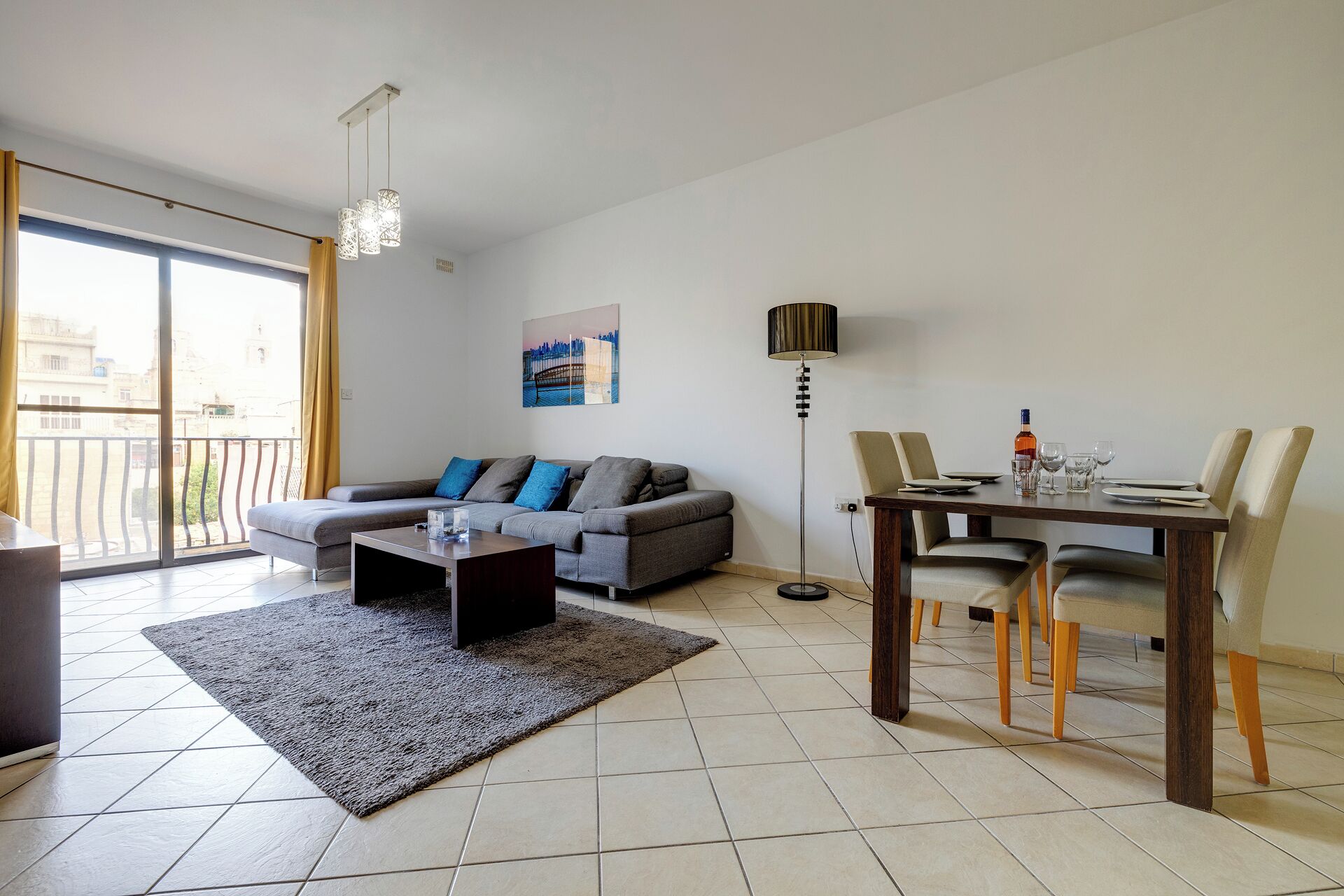 A modern living room with a grey sofa, a coffee table, and a dining table set for four.