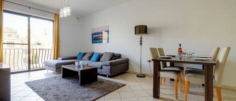 A modern living room with a grey sofa, a coffee table, and a dining table set for four.