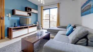 Ett modernt vardagsrum med en platt-TV, en TV-möbel i trä, en grå soffa och ett stort fönster med gardiner.