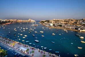 A marina with numerous boats docked, a clear sky, and a cityscape in the background. - Modern 2BR Sliema Apartment (Sliema)