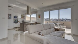 A modern living room with a large sofa, a kitchen with a central island, and a balcony with a city view. - Luxury 2 Bedroom Penthouse in St Julians (Swieqi)