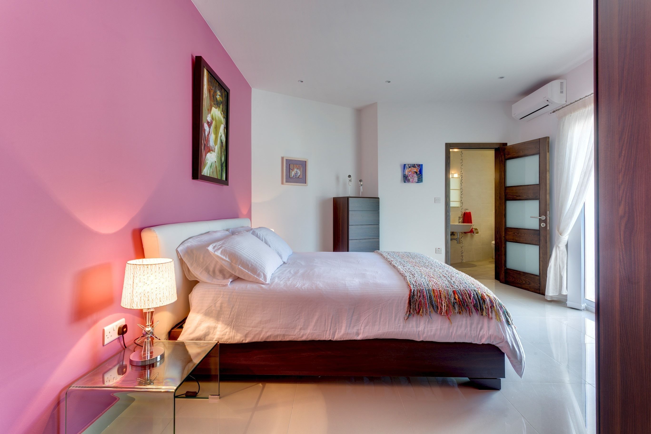 A bedroom with a bed, bedside table, lamp, and artwork on the wall.