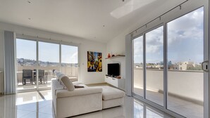 A modern living room with a sofa, a flat-screen TV, and a painting on the wall. - Luxury 2 Bedroom Penthouse in St Julians (Swieqi)