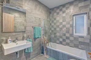 A bathroom with a white sink, a mirror, a towel rack, a shower, and a patterned tile wall. - Luxury 2 Bedroom Apartment by the Sea (St. Paul's Bay)
