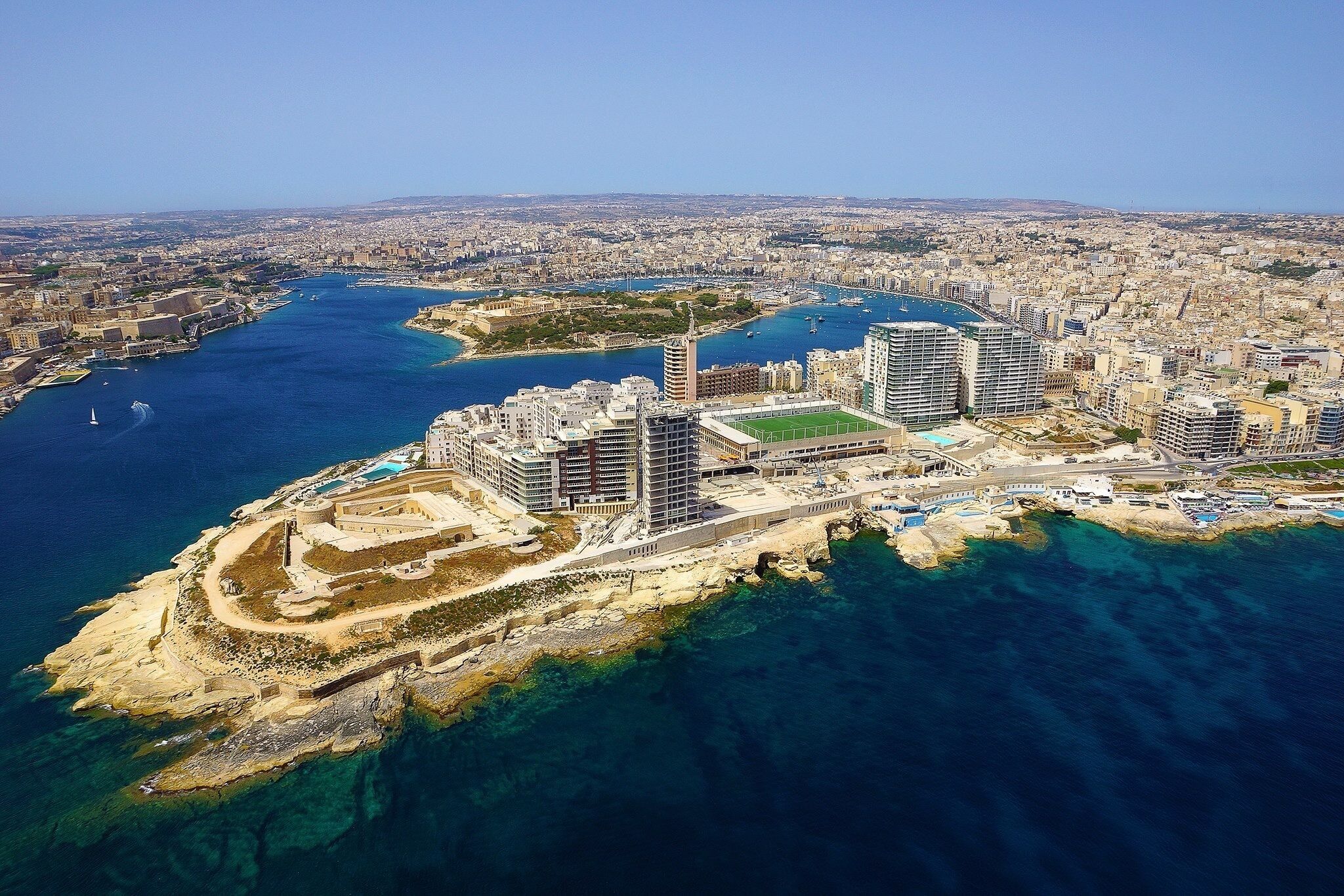 An aerial view of a coastal city with a prominent marina, high-rise buildings, and a sandy beach area.