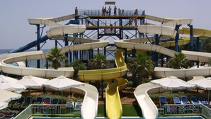 Een waterpark met meerdere glijbanen en een zwembadgedeelte met ligbedden en parasols.