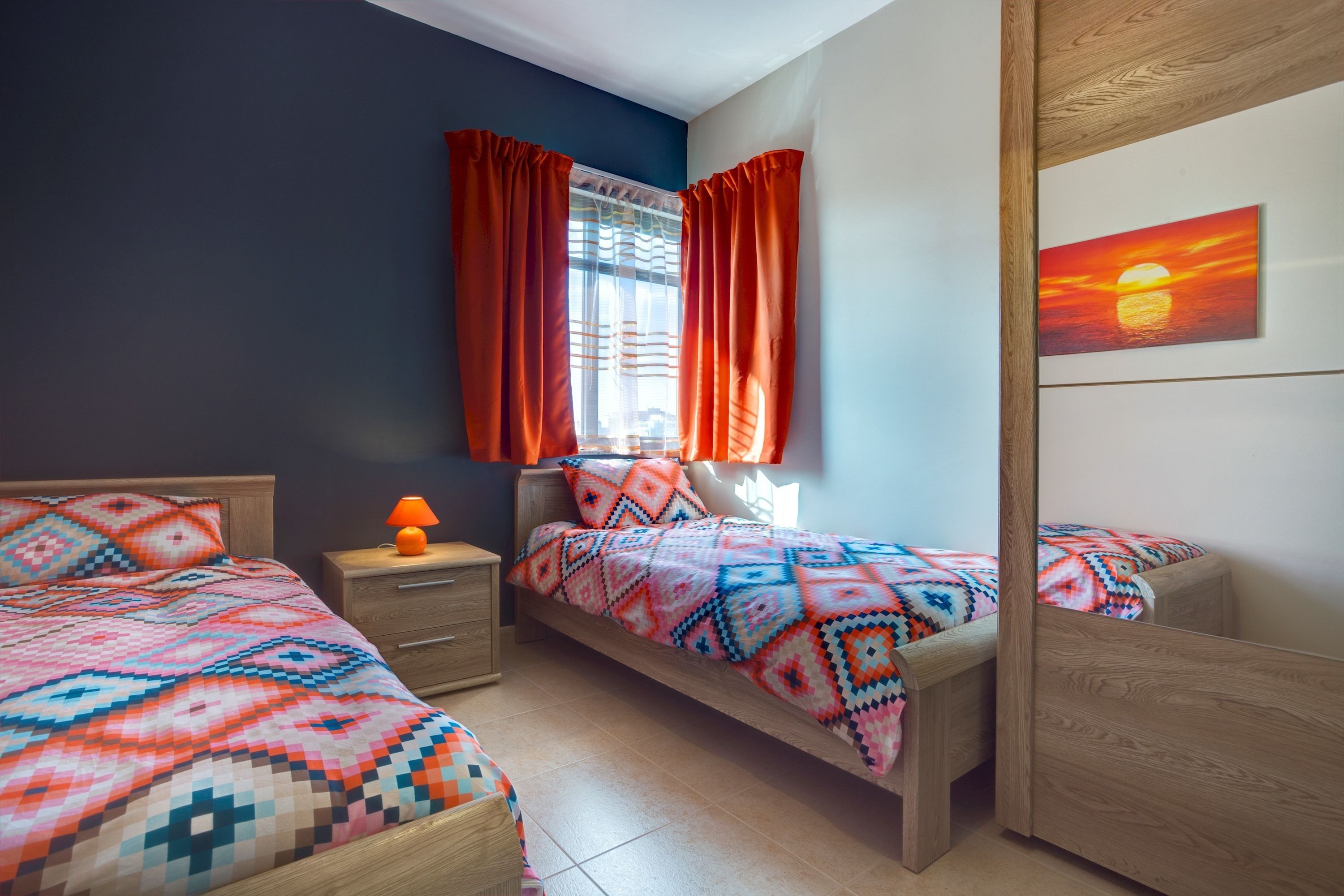 A bedroom with two beds, a nightstand, a lamp, and a window with curtains.