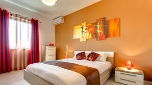 Een moderne slaapkamer met een groot bed, een nachtkastje, een wandairconditioner en een raam met rode gordijnen.