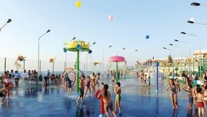 Een waterpark met diverse speelzones, waaronder glijbanen en fonteinen, omringd door veel mensen.