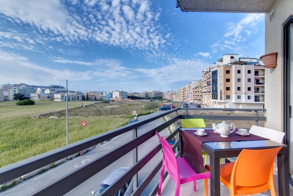 A balcony with a table set for tea, overlooking a road and buildings. - Modern Apt Overlooking Green Area (St. Paul's Bay)