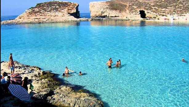 Helderblauw water met rotsformaties en mensen die zwemmen en zonnebaden.