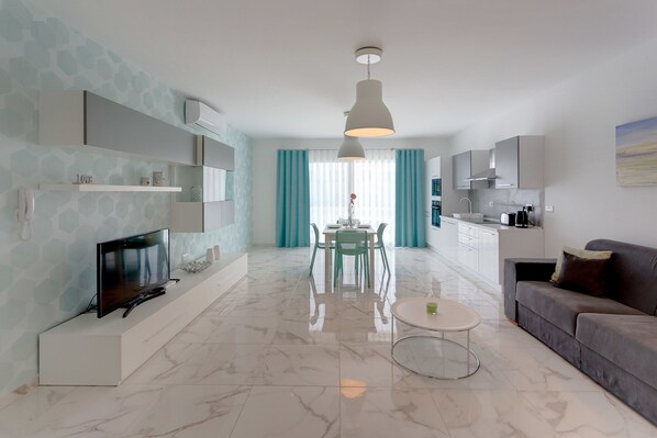 Uma sala de estar moderna com televisão, mesa de jantar e sofá.