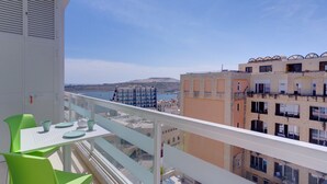 Un balcone con tavolo e sedie, vista su una località costiera con edifici e uno specchio d'acqua.
