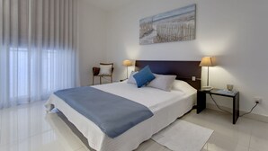 A bedroom with a large bed, two bedside tables, a nightstand, a chair, a painting on the wall, and a window with curtains. - Marvellous Apartment in Tigne Point With Pool (Sliema)