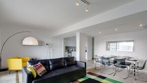 A modern living room with a black sofa, yellow armchair, and a dining area with a glass table and chairs. - Marvellous Seafront Apartment in the Best Location (Sliema)