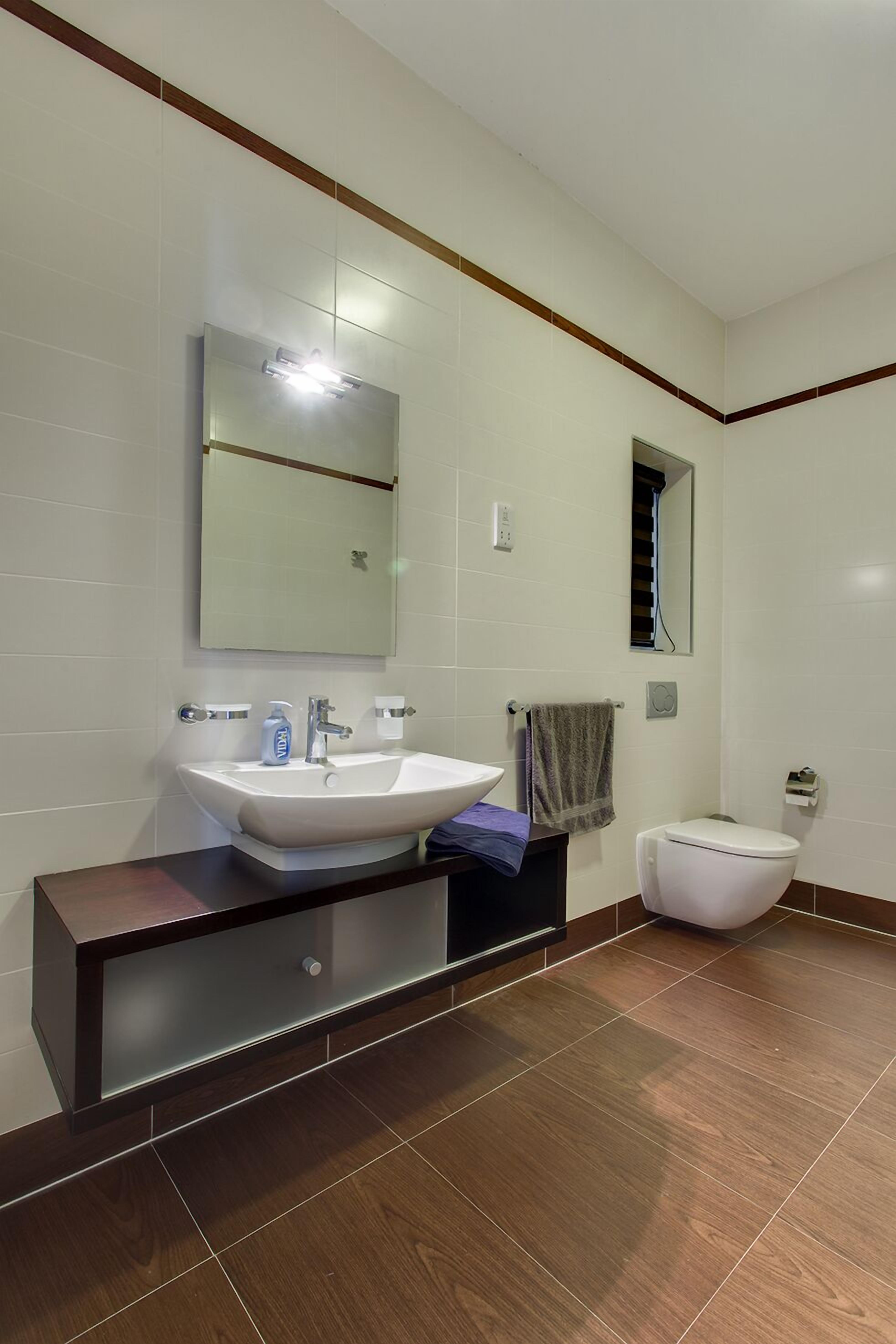 Un baño moderno con un espejo grande, un lavamanos blanco y un inodoro.